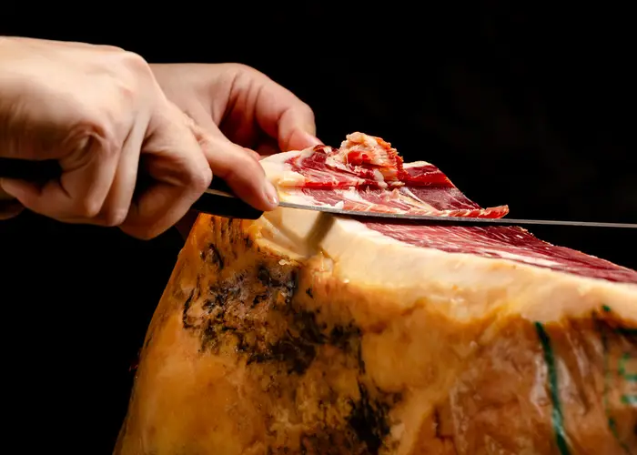Two hands slicing ham